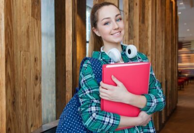 Smiling student holding book and wearing headphones, ready for study.