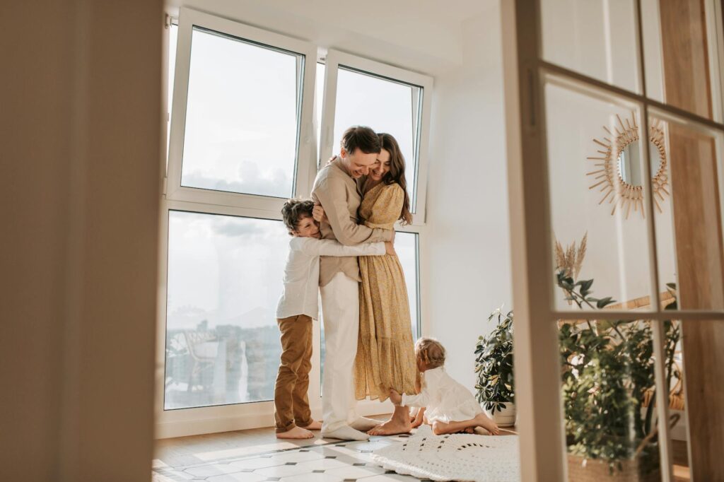 A happy family embracing near a large window in a bright, cozy room filled with natural light.