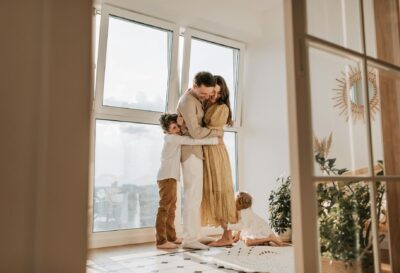 A happy family embracing near a large window in a bright, cozy room filled with natural light.